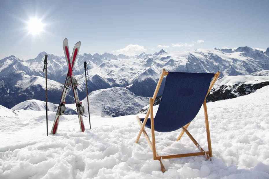 Skier im Schnee und ein Klappstuhl in der Sonne mit Ausblick auf die Berge im Winterurlaub